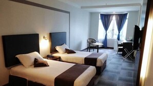 A hotel room with two beds, a desk, a chair, and a television.