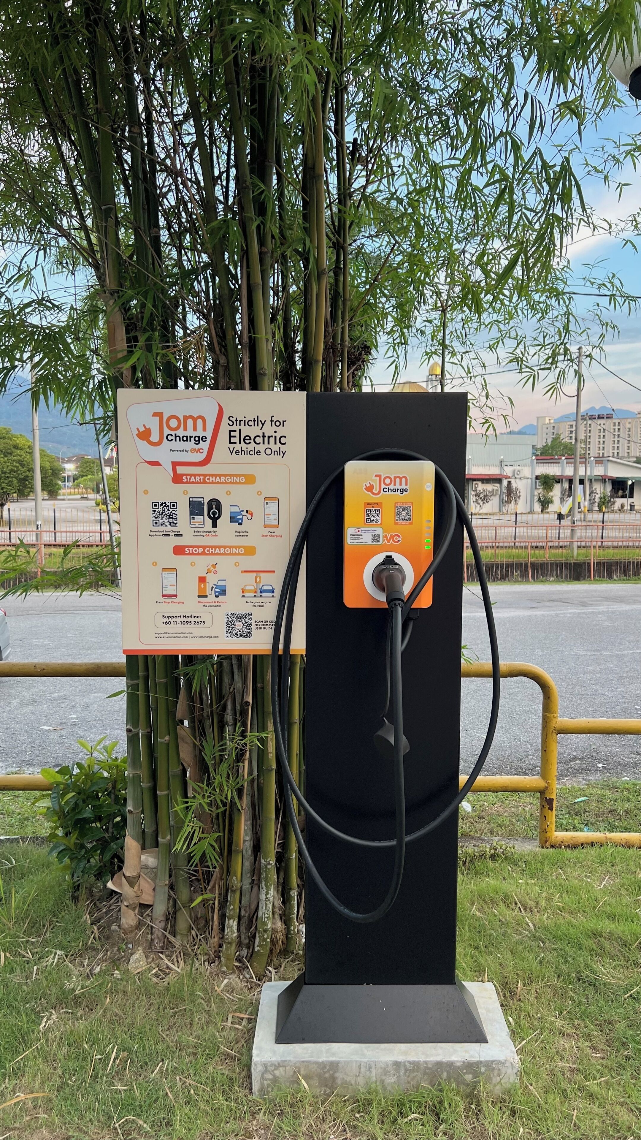 Una estación de carga para vehículos eléctricos, con un cartel que detalla el proceso de carga e información de contacto para soporte.