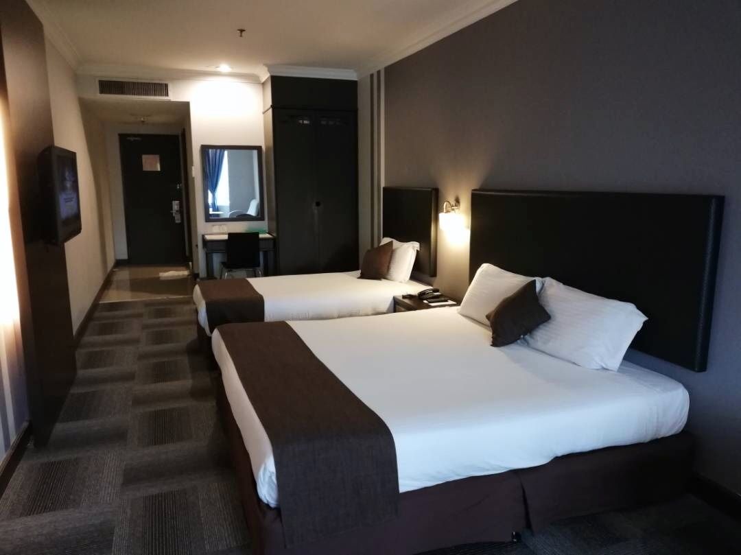 A hotel room with two beds, a desk, a chair, a TV, and a mirror.