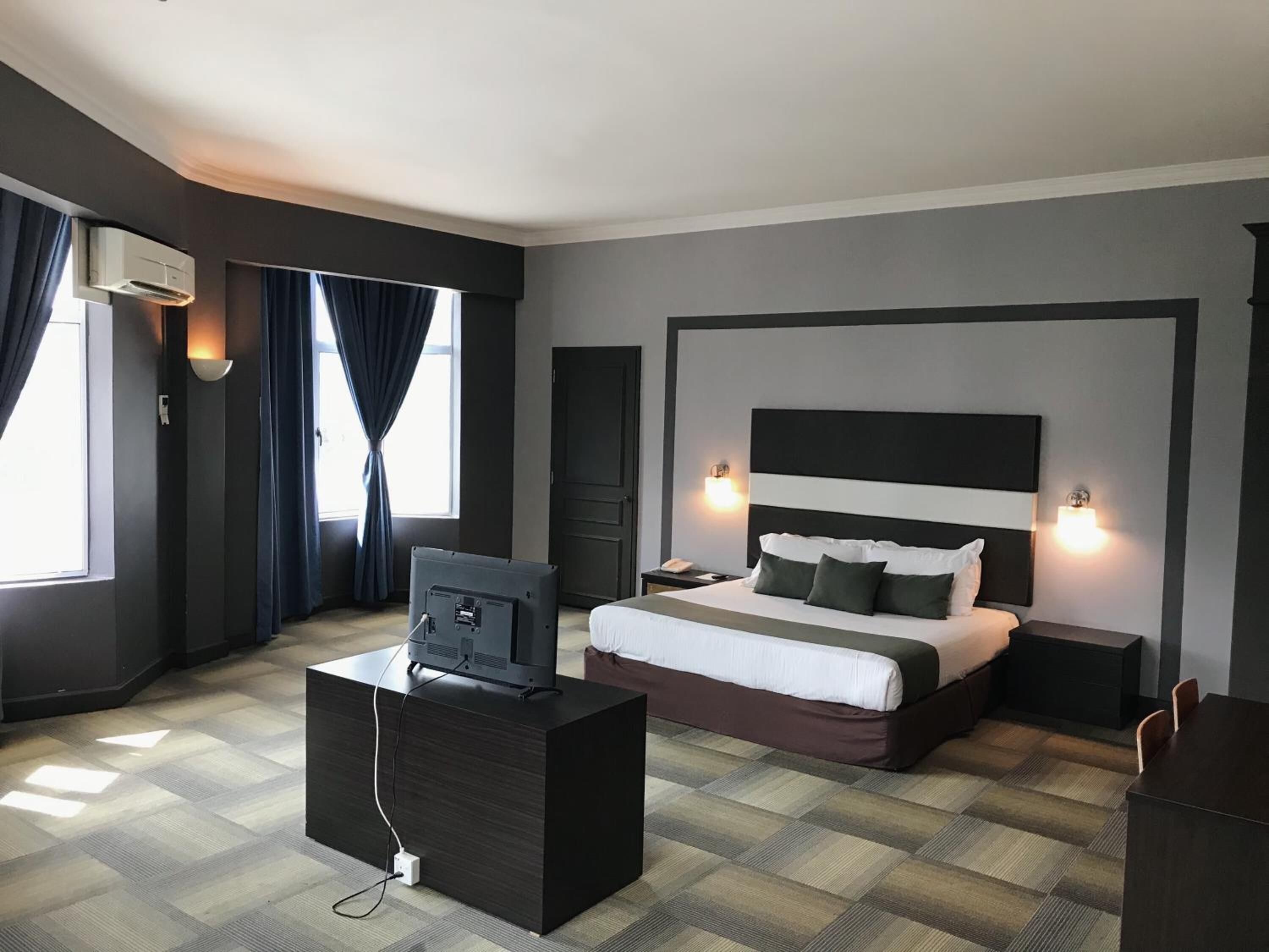 A hotel room with a bed, bedside tables, a TV on a stand, and a window with curtains.