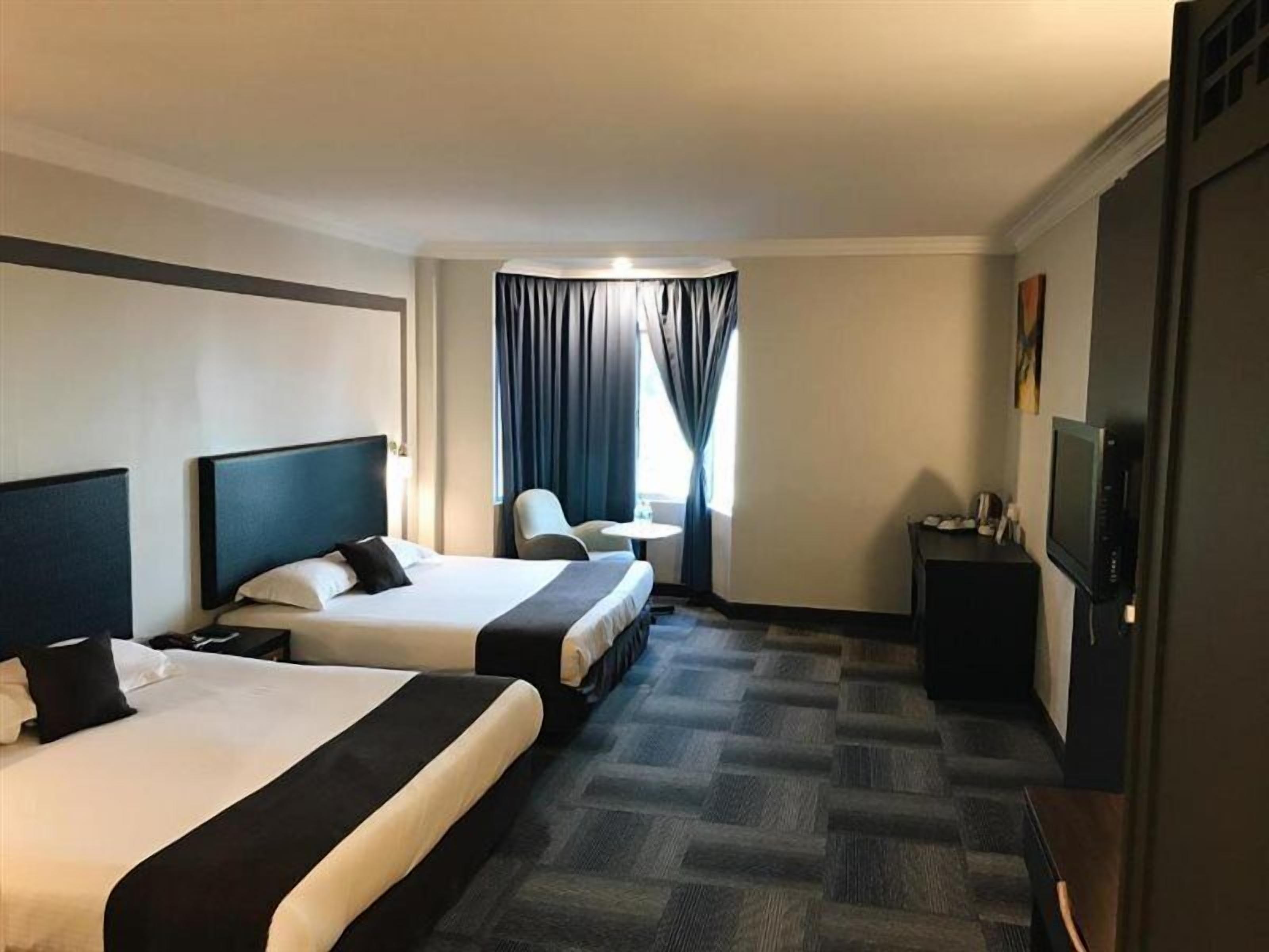 A hotel room with two beds, a desk, a chair, and a television.