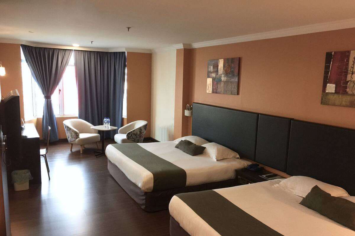 A hotel room with two beds, a desk, a chair, and a small table.