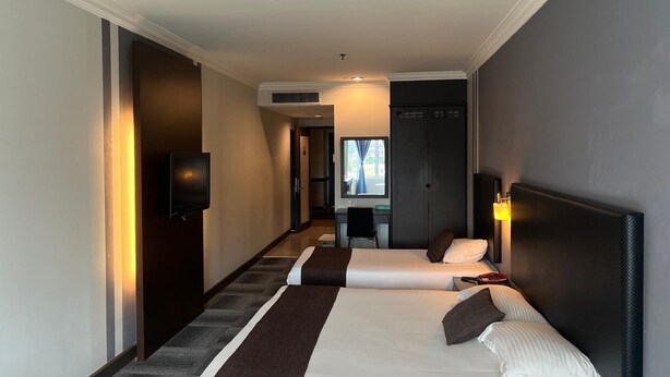Habitación de hotel con dos camas, un escritorio, una silla y un televisor.