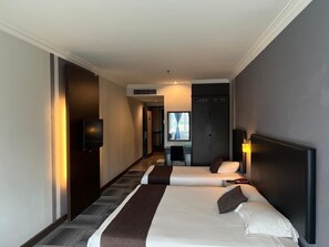 Habitación de hotel con dos camas, un escritorio, una silla y un televisor.
