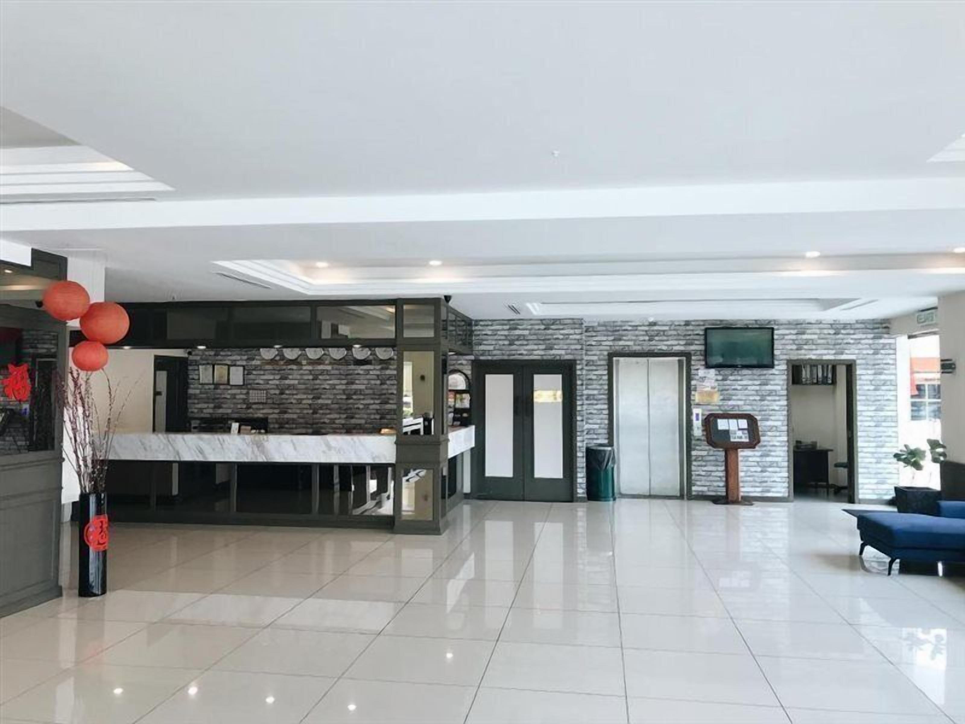 Un hall d’hôtel spacieux comprenant un comptoir d’accueil, un espace repas et un escalier menant à un étage supérieur.