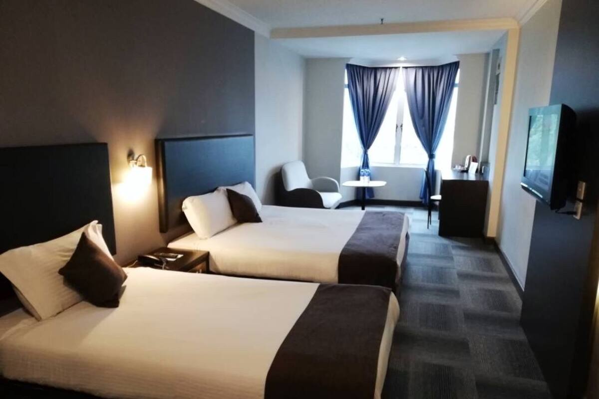 A hotel room with two beds, a desk, a chair, a TV, and a window with curtains.
