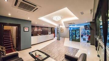 A hotel lobby with a reception desk, seating area, and a staircase leading to another floor.