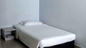 A single bed with a white mattress and pillow, a bedside table, and a wall-mounted shelf. - Century Hotel Inanam (Kota Kinabalu)