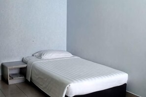 A single bed with a white mattress and pillow, a bedside table, and a wall-mounted shelf. - Century Hotel Inanam (Kota Kinabalu)