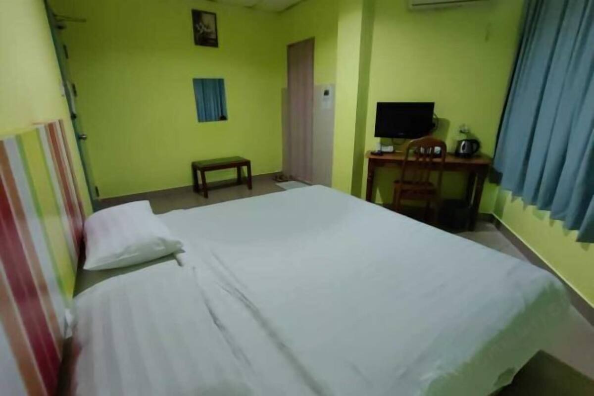 A room with a bed, a desk with a computer, a chair, a small table, and a television.