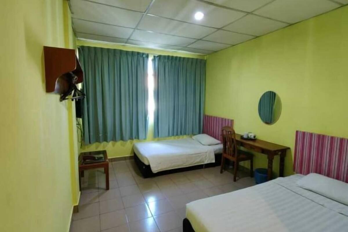 A room with two beds, a desk, a chair, a small table, a wall-mounted lamp, and a window with curtains.