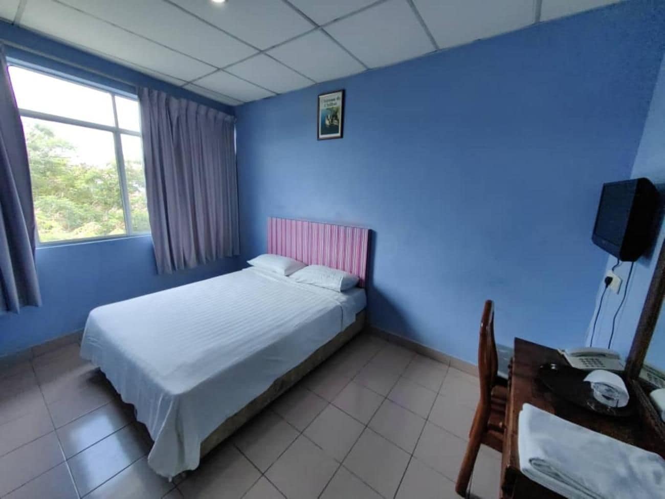 A hotel room with a bed, a desk with a telephone, and a window with curtains.
