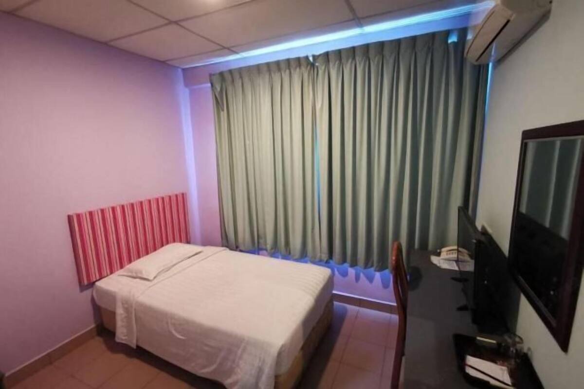 A hotel room with a bed, a television, a desk, and a window with curtains.