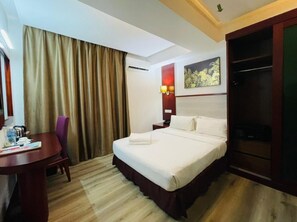 A hotel room with a bed, a desk, a chair, a wardrobe, and a painting on the wall. - Celyn City Hotel (Kota Kinabalu)