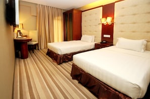 A hotel room with two beds, a desk with a lamp, a TV, and a large window with curtains. - Celyn City Hotel (Kota Kinabalu)