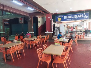 Un restaurant amb cadires i taules taronges, un cartell que indica 'Khalisah' restaurant, i una escala que condueix a un nivell superior.