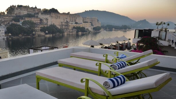 A rooftop terrace with sun loungers and a view of a historic cityscape and river. - Lake Pichola (Udaipur)