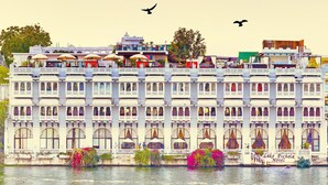 Un edificio a più piani con balconi, un cartello con su scritto 'Lake Pichola Hotel' e un corpo d'acqua antistante.