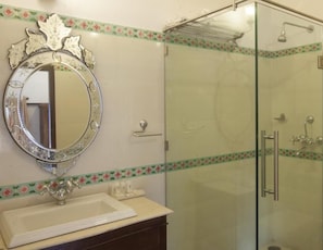 A bathroom with a glass shower enclosure, a sink with a decorative mirror, and a floral border on the walls. - Lake Pichola (Udaipur)