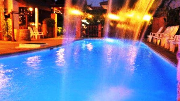 A swimming pool with water jets, surrounded by lounge chairs and a building with lights. - MD House (Chiang Mai)