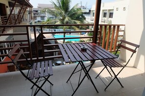A balcony with a wooden table and chairs, overlooking a swimming pool and palm trees. - Prince (Chiang Mai)