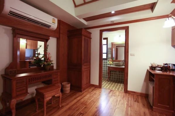 A room with wooden flooring, a built-in bench, a wooden cabinet, and a doorway leading to a bathroom with a tiled floor. - Rich Lanna House (Chiang Mai)