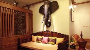 Una habitación con un sofá de madera, una cabeza de elefante decorativa montada en la pared y una mesita con un florero.