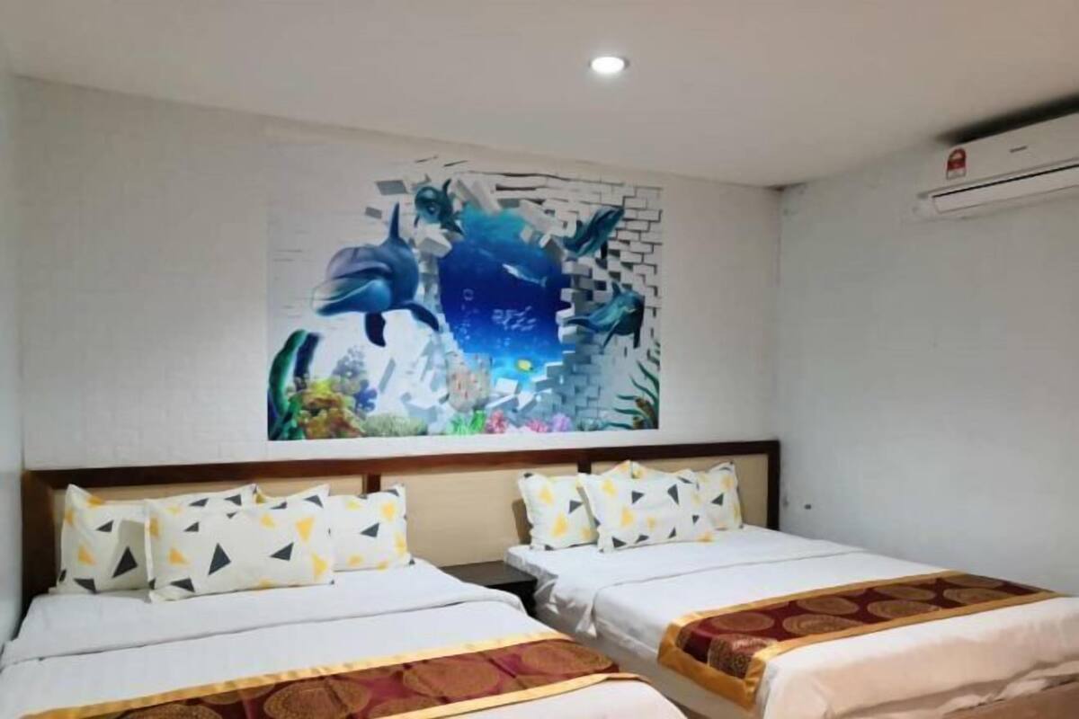 A hotel room with two beds, each with patterned pillows, a large wall mural, and a ceiling light.