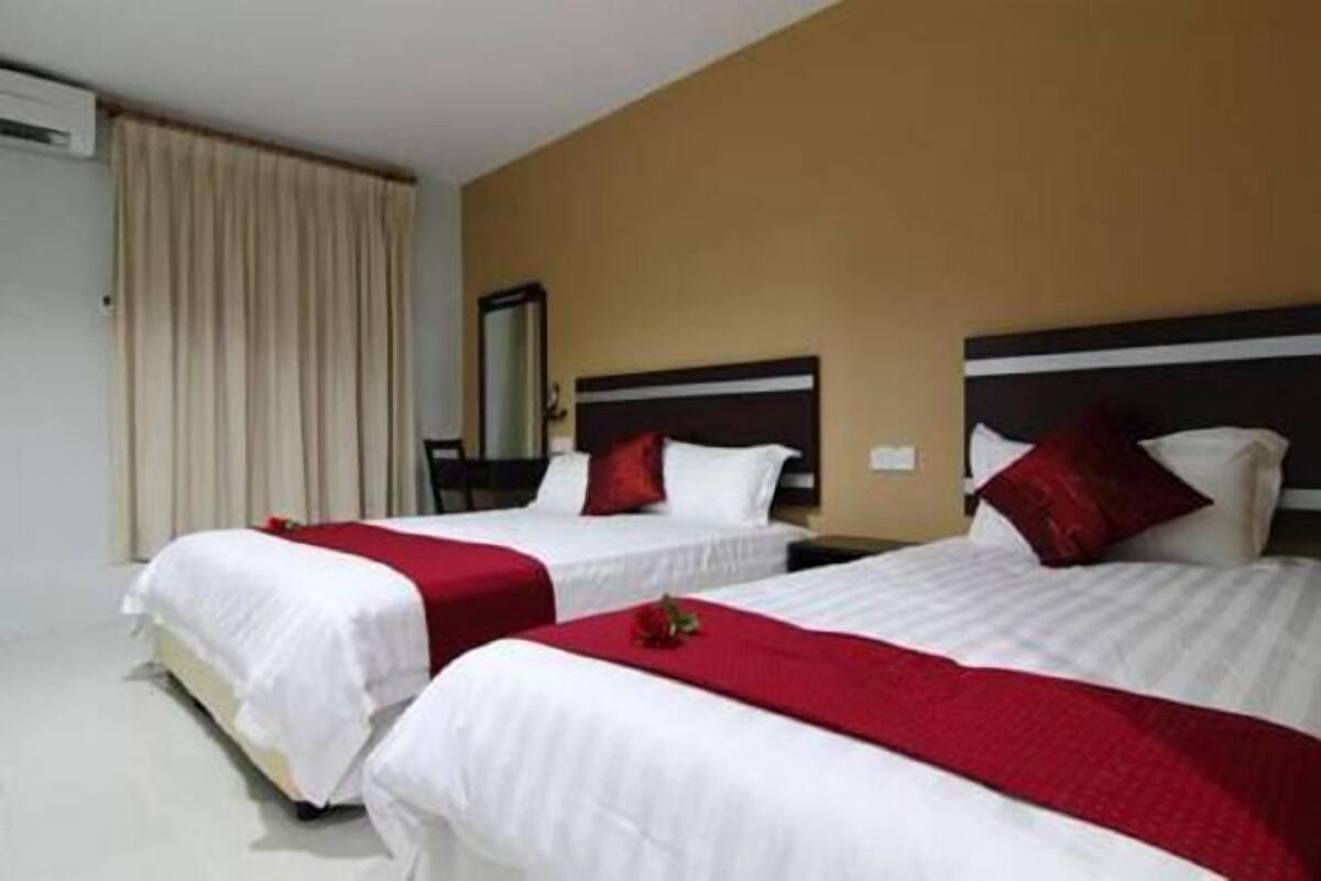 A hotel room with two beds, each with white bedding and red accents, a beige curtain, and a mirror on the wall.