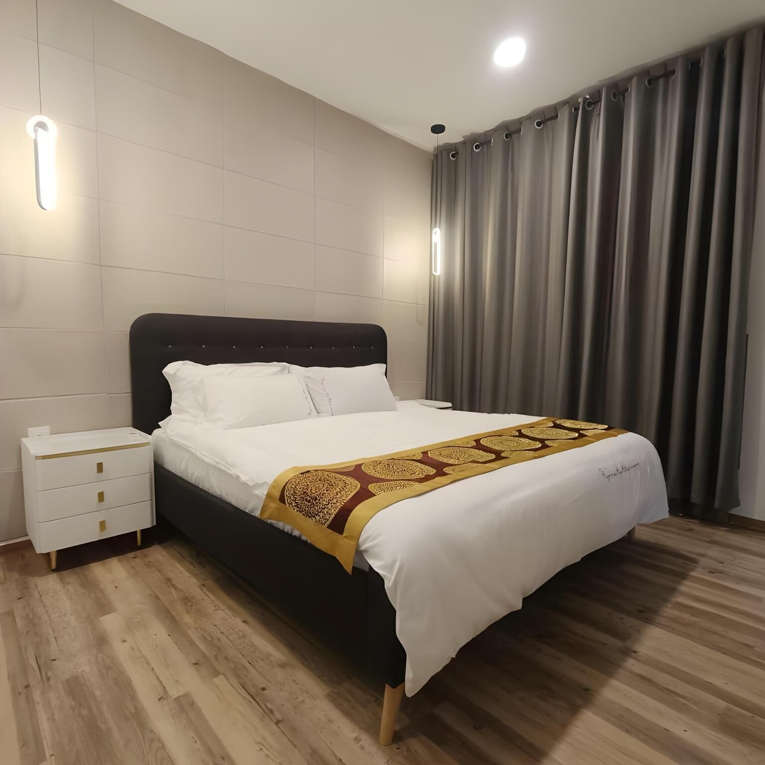 A bedroom with a bed, bedside tables, a headboard, curtains, and a ceiling light.