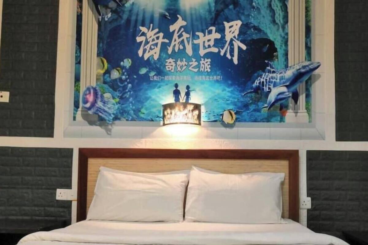 A hotel room with a bed, a wall mural of an underwater scene, and a wooden headboard.