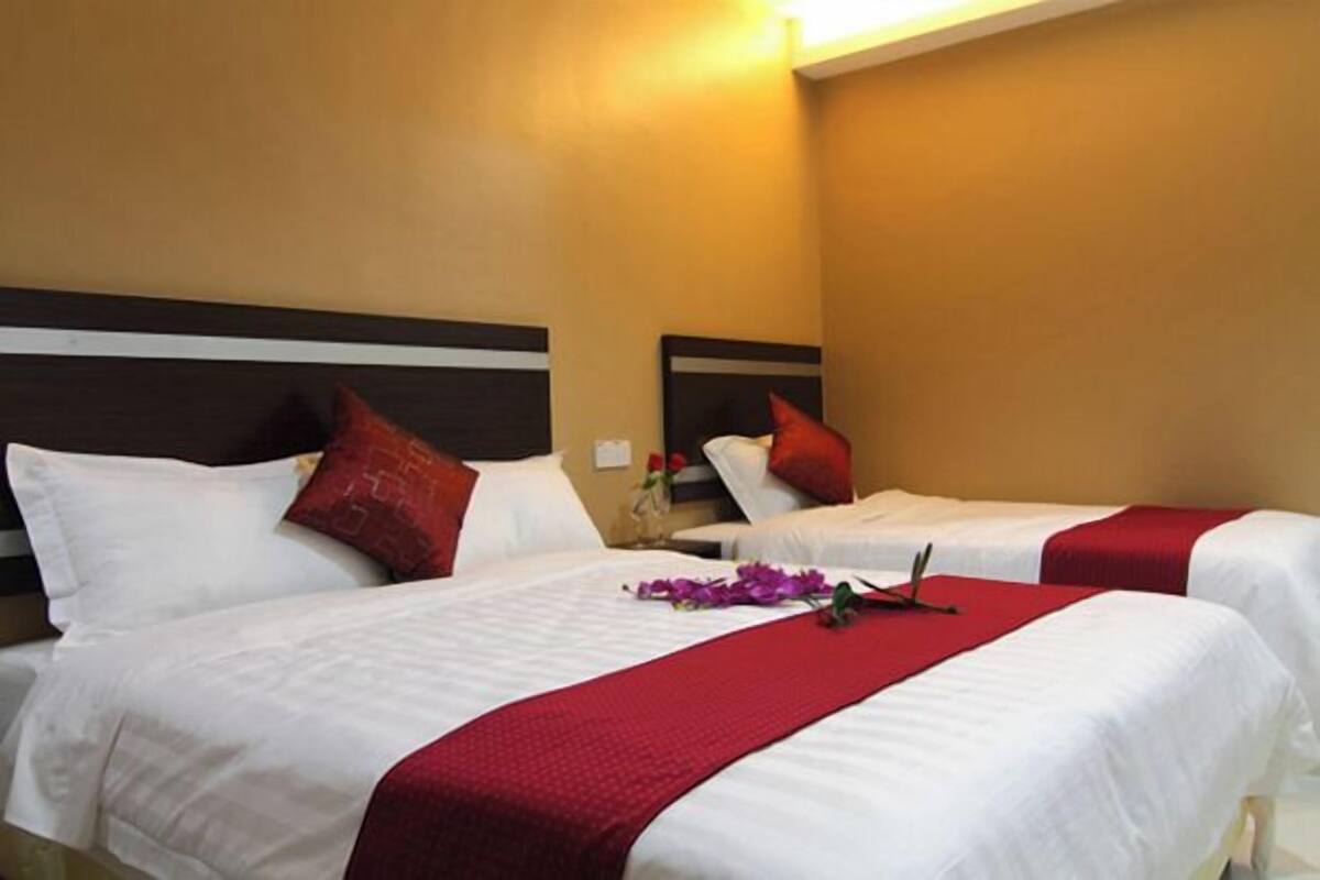 A hotel room with two beds, each with white bedding and red accents, and a mirror above the beds.