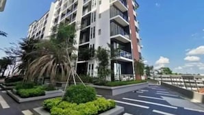 Un moderno edificio residencial de varios pisos con balcones, rodeado de vegetación cuidada y un cielo despejado.
