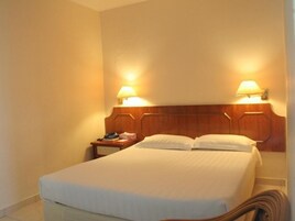Habitación de hotel con cabecera de madera, dos lámparas de noche, cama con ropa blanca y mesita de noche con un teléfono y un libro.