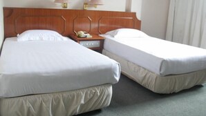 Habitación de hotel con dos camas individuales, cabecera de madera, lámparas de noche, mesita de noche con teléfono y ventana con cortinas.