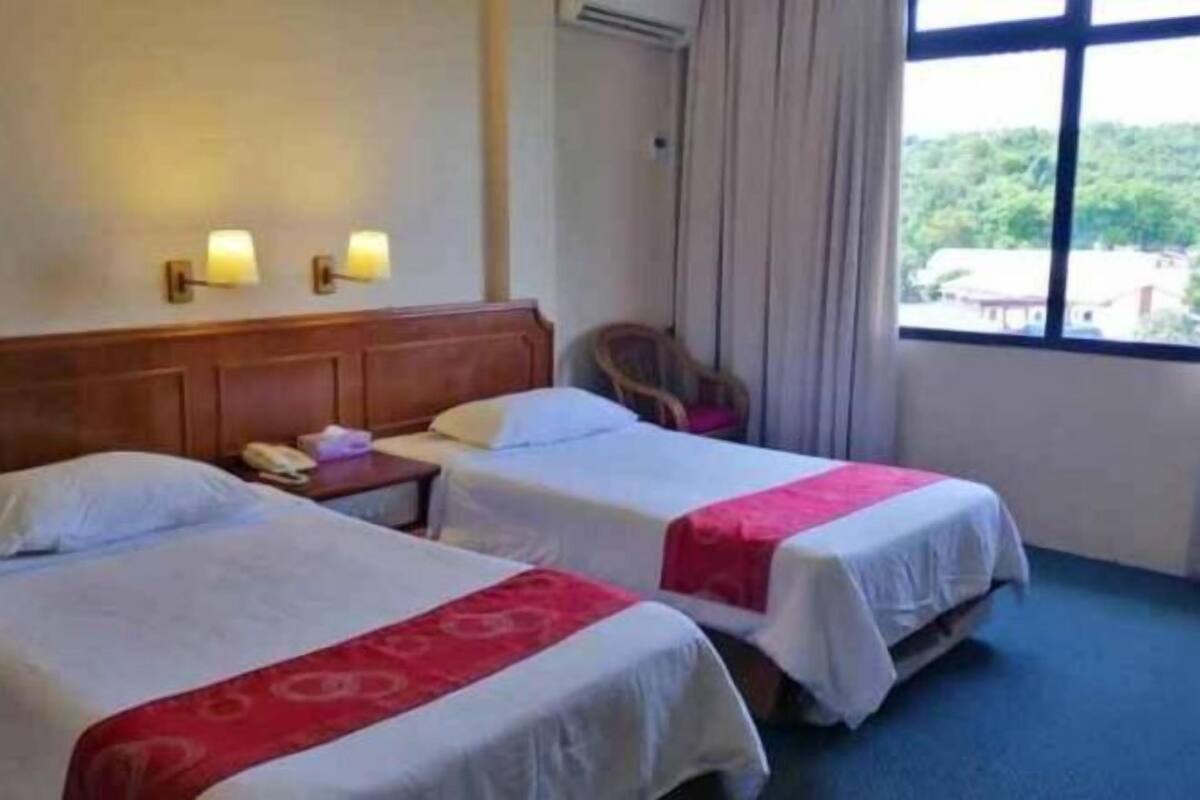 Camera d'albergo con due letti, una testiera in legno, un comodino con un telefono e una finestra vista verde.