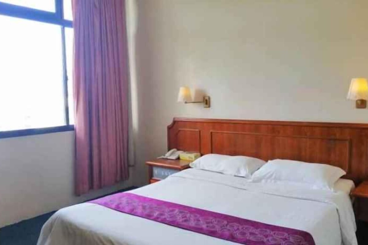 A hotel room with a bed, a nightstand, a lamp, and a window with curtains.