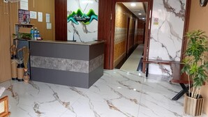 Een hotel receptie met een marmeren vloer, een receptiebalie en een bordje met 'Bate Cares Business Hotel'.