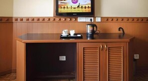 Ett träskåp med en platt-tv monterad ovanpå, en kaffebryggare och ett bricka med koppar och en sked.
