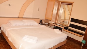 A hotel room with a large bed, a wooden headboard, a bedside table with a lamp, and a mirror. - Hilltop Towers Kodaikanal (Kodaikanal)