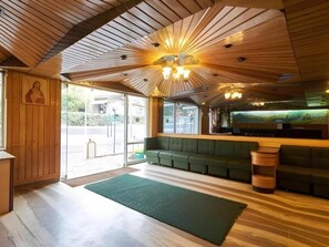 Un espace d’accueil doté d’un plafond en bois, d’un canapé vert et d’un comptoir de réception.