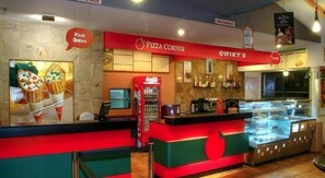 En pizzarestaurangs interiör med en bardisk, menytavlor och ett kylskåp med Coca-Cola.