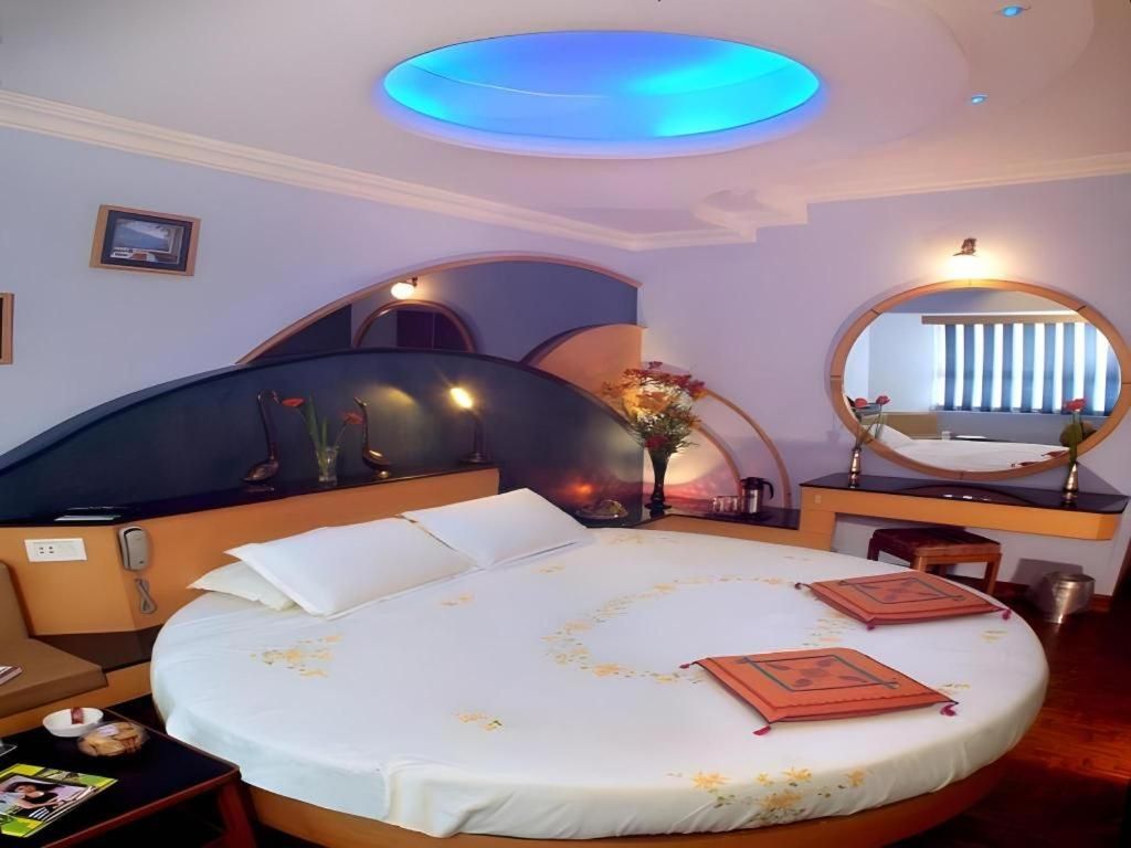 A hotel room with a round bed, a desk with a mirror, and a ceiling light.