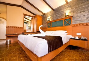 A hotel room with a large bed, wooden headboard, stone wall, and a wooden cabinet. - Hilltop Towers Kodaikanal (Kodaikanal)