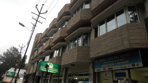 A multi-story building with balconies, a sign for Hilltop Zoopads, and a travel agency named Kurinji Tours and Travels. - Hilltop Towers Kodaikanal (Kodaikanal)