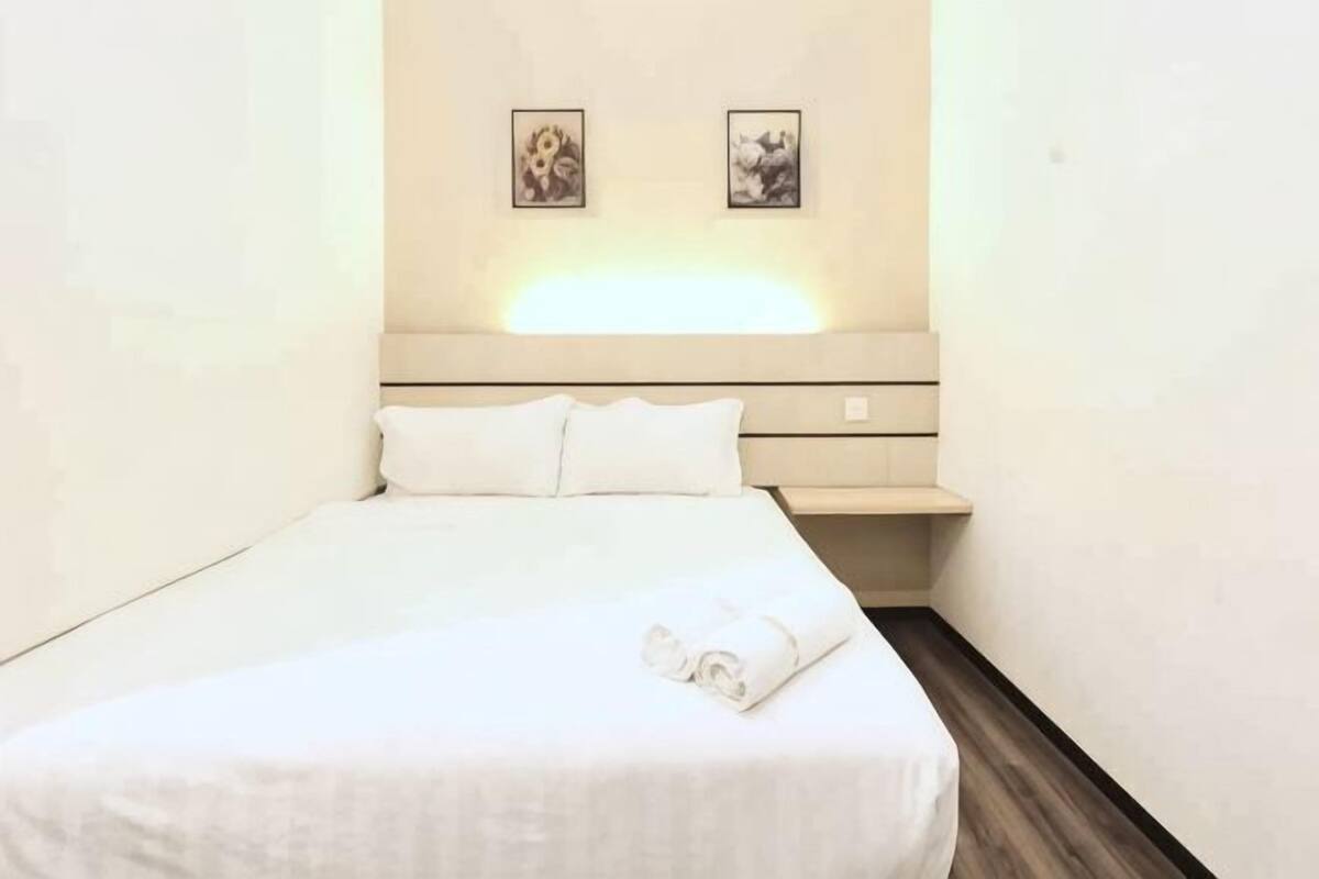 A neatly made bed with white linens and a rolled towel, a bedside table, and two wall-mounted pictures.