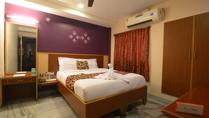 A hotel room with a bed, bedside table, mirror, wardrobe, and an air conditioning unit. - Hotel Vijay (Madurai)