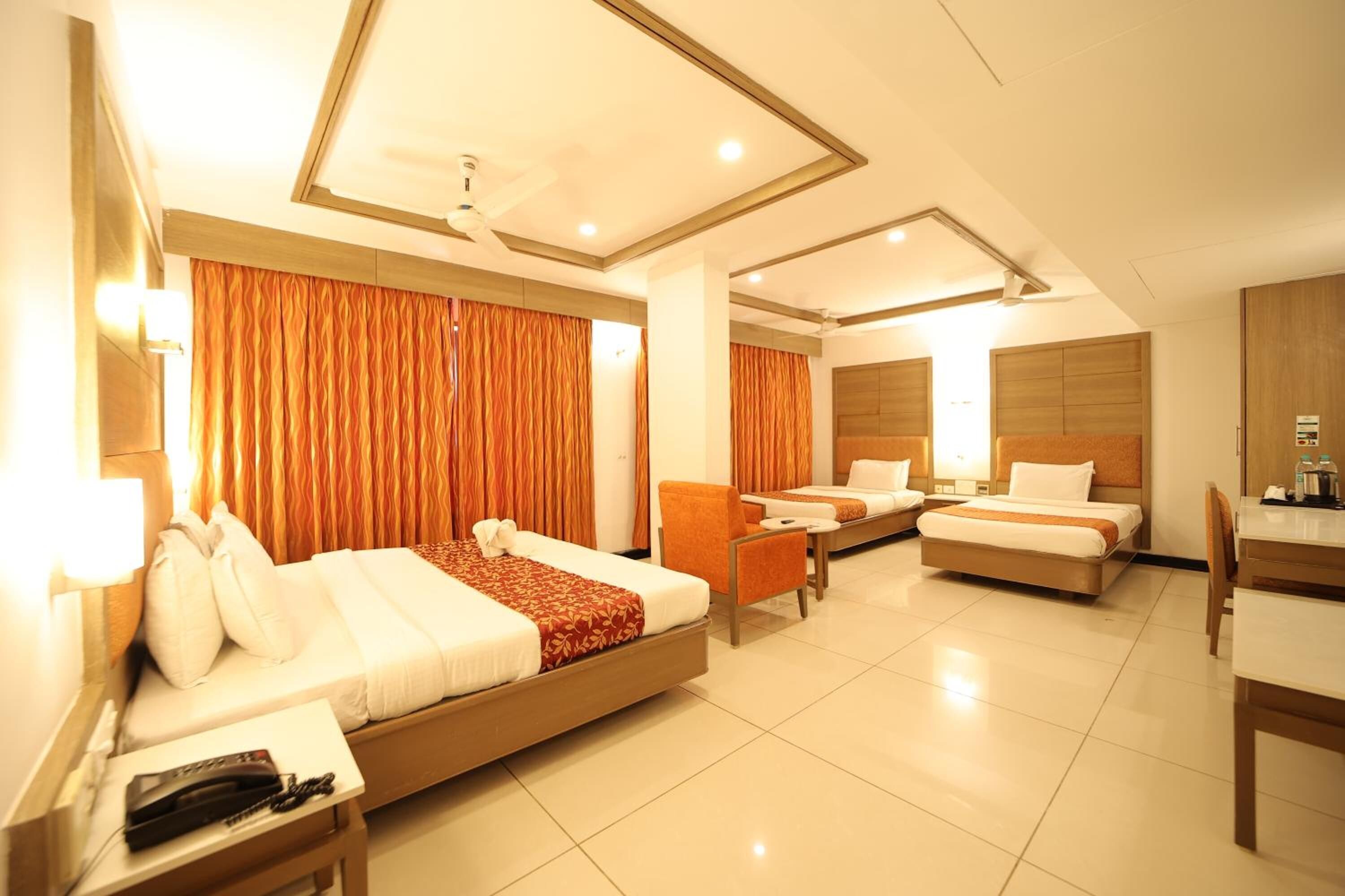 A hotel room with a large bed, two smaller beds, a desk, and a chair.