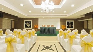 A conference room with rows of white chairs with yellow sashes, a green table with a white tablecloth, and a chandelier. - Clinton Park Inn (Nagapattinam)