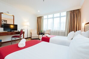 Two large beds with crisp bedding, a desk with a flat-screen TV, and a comfortable chair.
